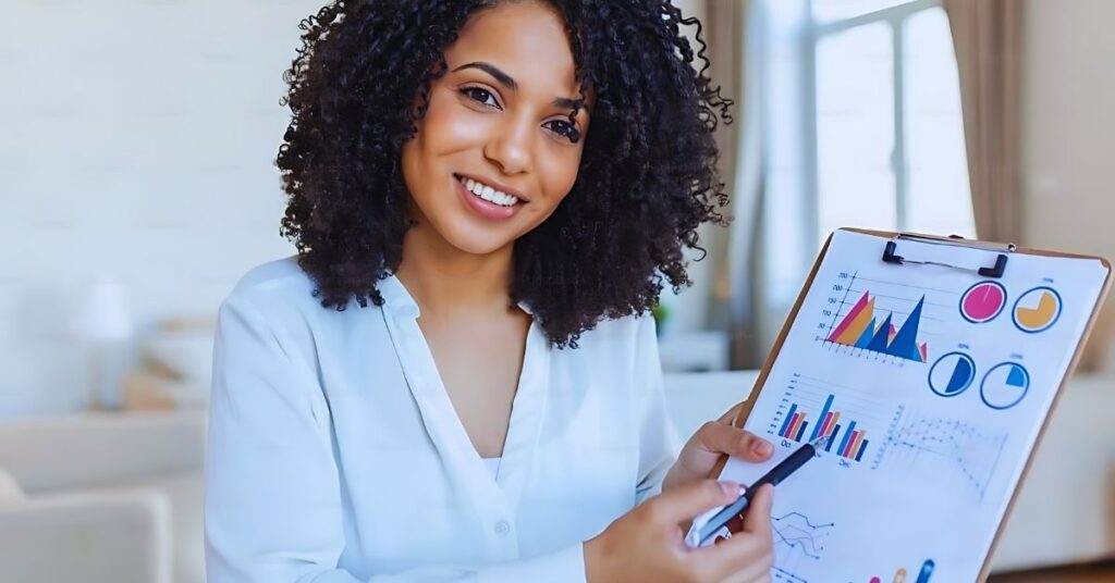 "A smiling professional woman holding a clipboard displaying colorful charts and graphs. She points to a specific section with a pen, emphasizing data insights and analytics. The background is a bright, modern room, suggesting a professional yet approachable setting for data analysis and presentation."